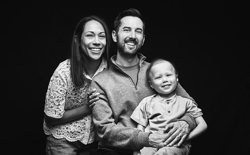 Black and white image of smiling young parents holding their young child.