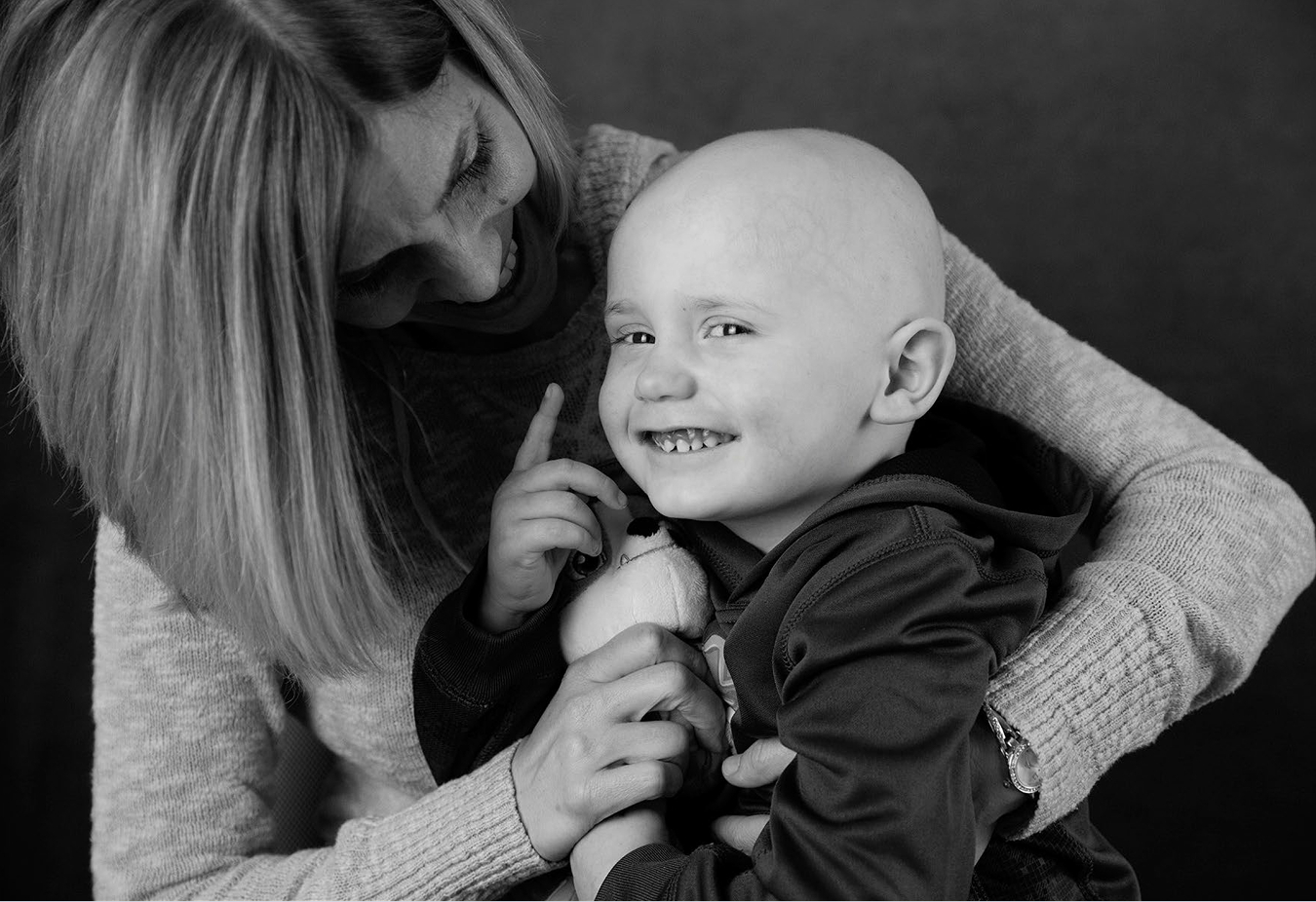 A mom hugs her young child, who is smiling and bald